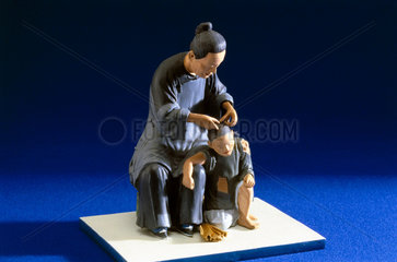 Figurine of a Chinese woman examining a child for head lice.