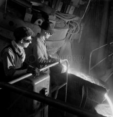Molten metal flows as figures tap a carbon arc furnace  1951.