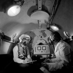 Two men with high alititude oxygen masks making tests in altitude chamber.