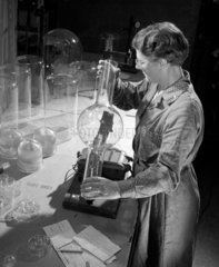 Female worker inspects a glass envelope for a mercury vapour lamp.