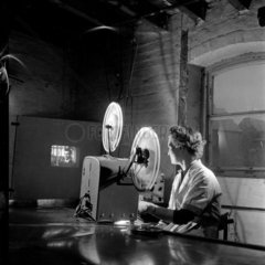 Female factory worker runs a 16mm projector to make final tests  1953.