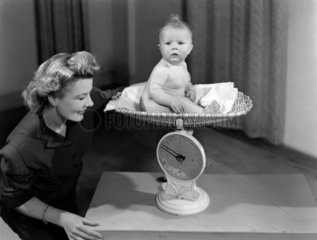 Woman weighing a baby on a pair of scales  c 1949.
