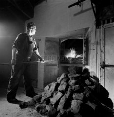 A distillery man prepares a peat fire used in furnace to heat containers.