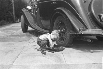 Young child making adjustments to the rear wheel of a Riley saloon car  c1930s.