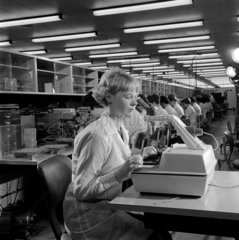 Female worker in foreground of line inspecting semiconductors  1967.