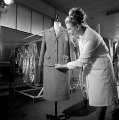 A female tailor fits a finished women's two piece suit over manequin  1966.