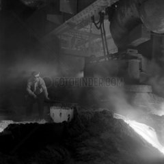 A steelworker taps slag off running molten metal  Consett  1957.