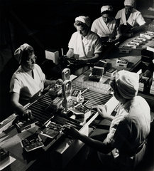 Women at conveyor belt packing boxes of Good News chocolates  1961.