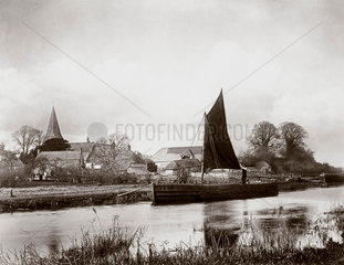 Sailing boat moored by a village  c 1890s.