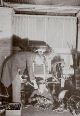 C S Rolls (standing) instructing a mechanic working in a garage  c 1900.