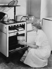 Woman taking a cake from an oven  1954.