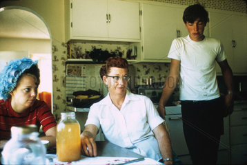 Two women and a teenage boy in a kitchen  United States  1972.