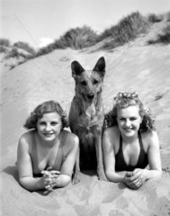 Dog flanked by two women  c 1930s.