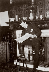C S Rolls standing by a fireplace reading  c 1900.