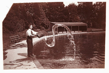 Man throwing a bucket of water into a pond  c 1905.