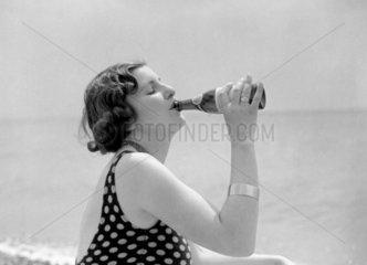 Woman in a bathing costume drinking Schweppes by the sea  c 1920s.