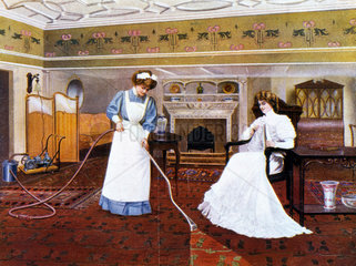 Maid vacuuming whilst seated lady looks on  1911.