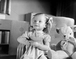 Little girl sitting with a teddy bear  c 1950.