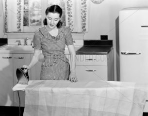 Woman ironing in the kitchen  c 1940s.
