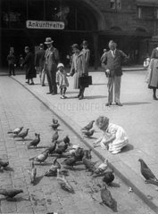 Little girl feeding pigeons in a German market square  c 1920s.