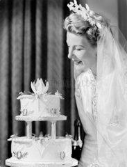 Smiling bride looking at her wedding cake  c 1948.
