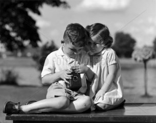 Two children inspecting a box camera  c 1930s.