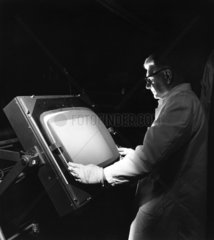 A production worker inspects a cathode ray tube shadow mask 1967.