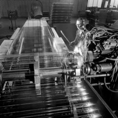 Worker at forming machine with rows of finished glass tubes on line  1964.
