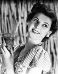 Smiling young woman holding a drink  c 1940s.