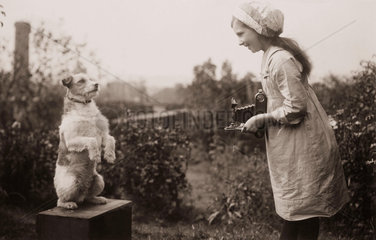 Young girl taking a photograph of a dog  c 1920s.
