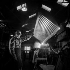 A CO2 welding fitter holds a radiator while his colleague spot welds the end .