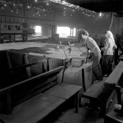 Two female workers tend sheets of steel in plate mill  Consett Iron Company.