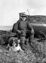 Fisherman and his dog next to a boat  c 1910s.
