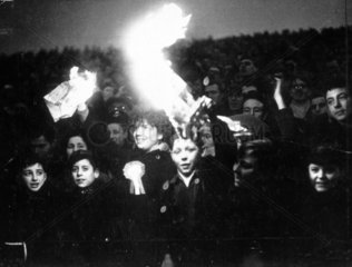 Spectators holding lit newspaper flares.