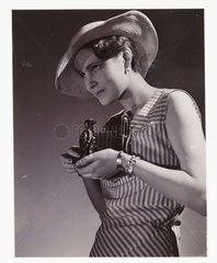 Woman in hat taking photograph using a folding roll film camera  c 1920s.