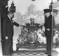 Two men inspecting Royal coat of arms  c 1965.