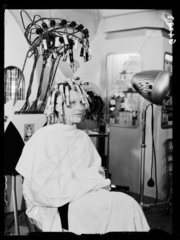 Woman sitting under a hair-curling machine  1938.