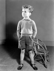 Boy standing next to a chair  c 1950.