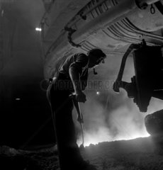 A furnaceman clears molten metal as it pours from a tapped blast furnace  1948.