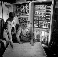 Engineers discuss plans in front of the electronic control panel they have built.