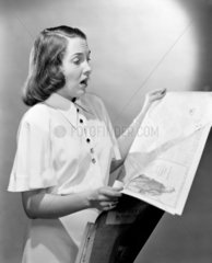 Woman looking shocked as she reads a newspaper  c 1950.