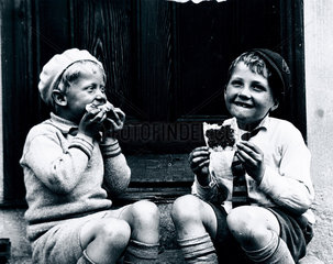 Two boys sitting on a doorstep eating bread and jam  c 1920s.