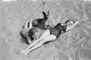 Two women and a dog on the beach  c 1930s.