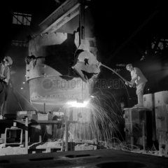 A man in the roll foundry purs molten metal in to a mould. 1960.