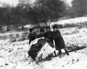 Schoolboys rolling a giant snowball  c 1930s.