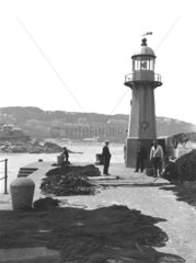 Fishermen mending nets by a lighthouse  St Ives  Cornwall  c 1920.