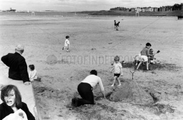 Group of children building sandcastles and playing cricket on the beach  1967.