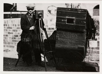 Photographer with tripod-mounted plate camera and other equipment  c 1890s.