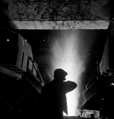 Steel worker silhouetted against furnace flames  Workington  1952.