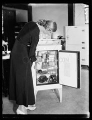 Woman taking milk from an electric refrigerator  1933.
